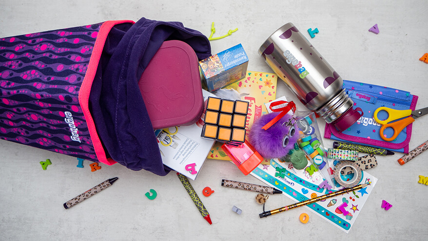 Aus eine lila-pink gemusterten Schultüte von ergobag quellen jede Menge Geschenke heraus: Spiele, eine Brotdose und Trinkflasche, ein Spitzer, ein Zauberwürfel, ein 3D-Puzzle sowie verschiedene Stifte und Radiergummis. Foto: Johanna Rundel