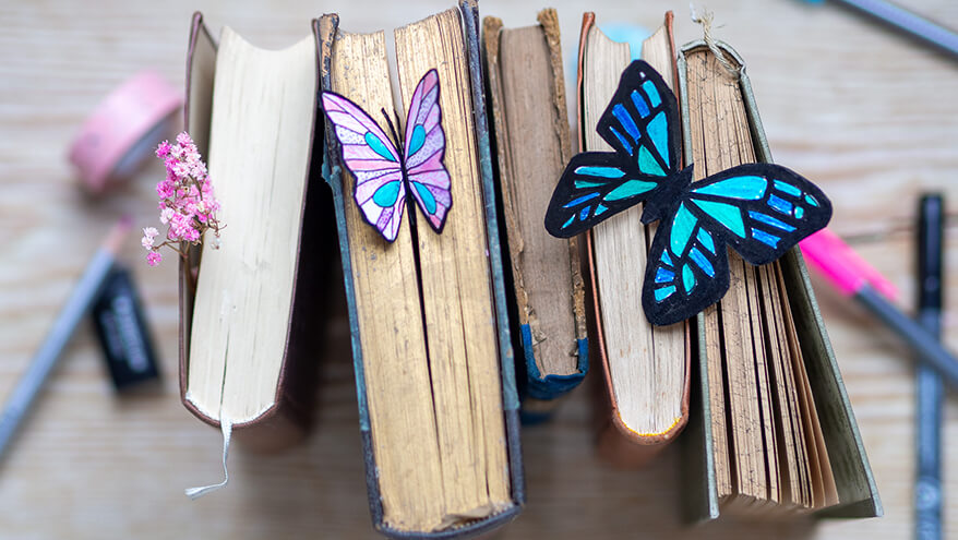 Eine Reihe hochkant gestellter, alter Bücher. Im Buchschnitt stecken zwei Lesezeichen in Schmetterlingsform. Foto: Johanna Rundel